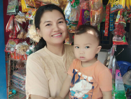 une bénéficiaire de Sont Oo Tehtwin pose devant sa boutique, avec son bébé dans les bras