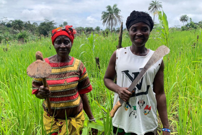 deux agricultrices bénéficiaires d'Elili sont dans un champ et tiennent dans la main leurs outils d