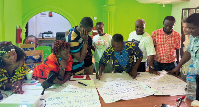 Groupe de personnes debout autour d'une table couverte de grandes feuilles manuscrites, lors d'un a